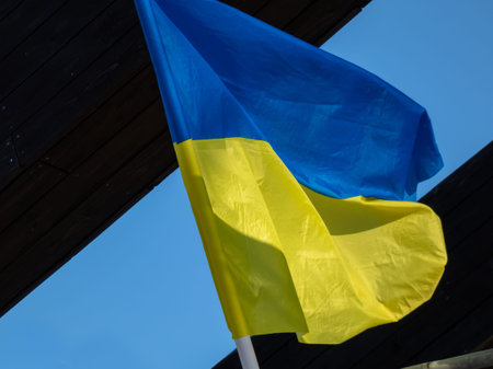 The blue and yellow Ukrainian flag flying in the sky on the flagpole near the building wall in...
