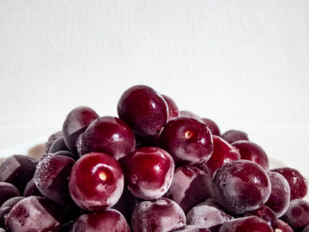 Macro shot of Frozen sweet, ripe cherry berries covered with white and melting hoarfrost on white plate with white background in bright sunlightの写真素材