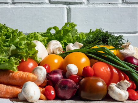A pile of fresh, healthy and colorful vegetables in bright sunlight with white brick wall in background. Tomatoes, onions, carrots, peppers, cauliflower, salad, dill and champignons on tableの写真素材