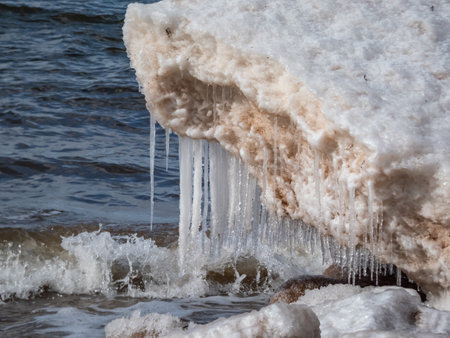 Close-up shot of the snow, ice and icicle formations in Baltic sea water on the shore in bright sunlight. Frozen ice blocks and sea water in winterの写真素材