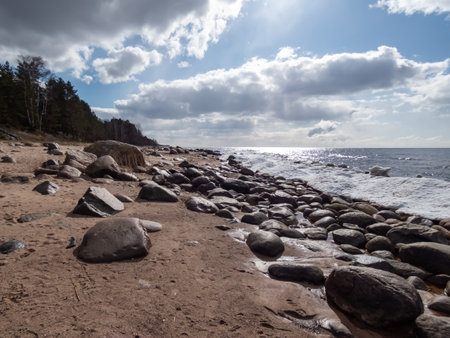 Seascape of Baltic sea and beach with big rocks with ice and snow formations on the shore in bright sunlight. Frozen ice blocks and sea water in winterの写真素材
