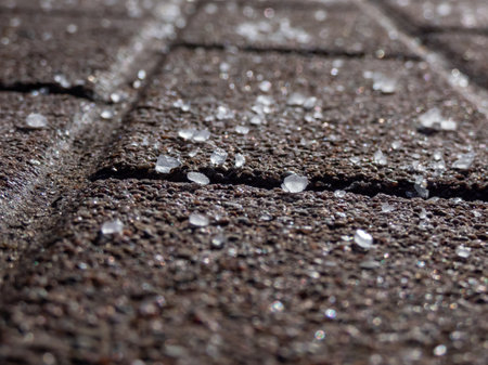 Close-up of white salt grains on icy sidewalk surface in the winter. Applying salt to keep roads clear and people safe in winter from ice or snow.の写真素材