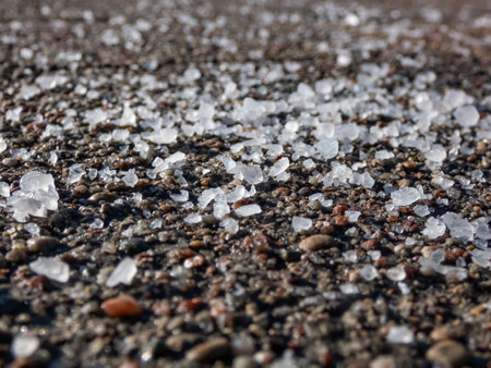 Close-up of white salt grains on icy sidewalk surface in the winter. Applying salt to keep roads clear and people safe in winter from ice or snow.の写真素材