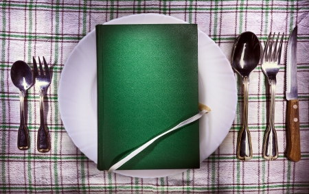 Old green book on white plate, accessories on both sides  Conceptual image of a book as food  の写真素材