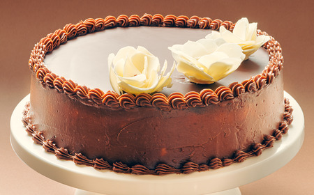 All chocolate birthday cake, on brown background, decorated with yellow flowers on top  の写真素材