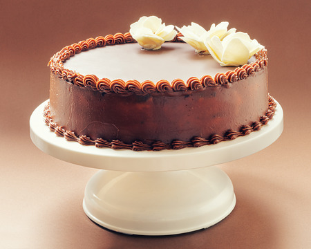 All chocolate birthday cake, on brown background, decorated with yellow flowers on top  の写真素材