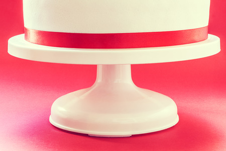 White round cake on red background, decorated with red ribbon  の写真素材