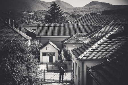 An old person standing and waiting for someone, or looking who is out on the street. Conceptual composition about life of an old persons in one of Balkan city. This photo also represents classical architectural style nowadays in Serbia.の写真素材