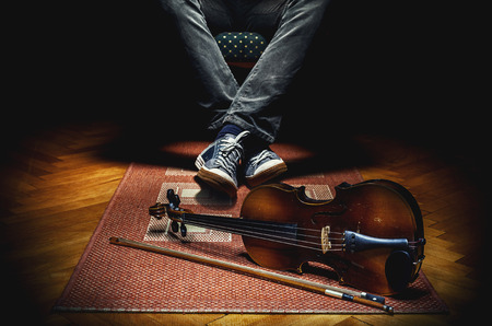 Violin player resting in armchair and his violin on tiled carpet.の写真素材
