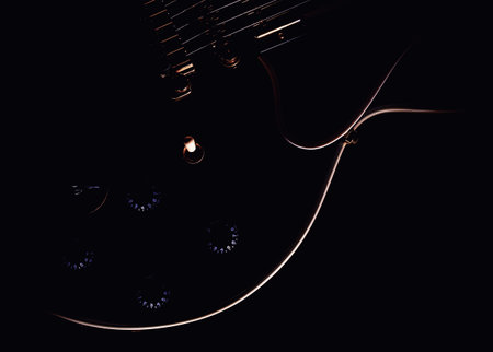 Body of electric guitar, black wood and white shapes accentuated with light.