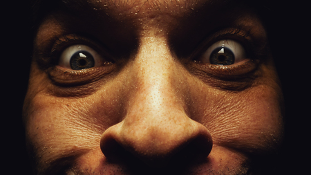 Surprised eyes of a male face, dark atmosphere, details and closeup view on eyes and skin.の写真素材