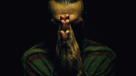 Man is praying, dark ambient, coupled hands and dark face.