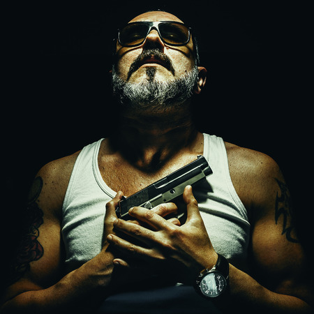 Relaxed and strong man holding a silver pistol on his chests.の写真素材