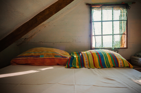 Interior of an old wooden loft, sunny day, dreamy ambient. Colorful pillows behind the window.の写真素材