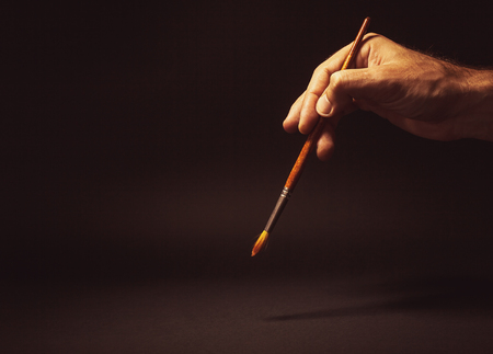 Conceptual composition, man's hand holding a brush on black background.の写真素材