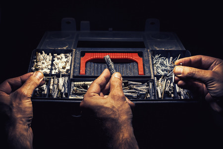 Old suitcase for nails, anchors and screws and three male hands choosing what to use.の写真素材