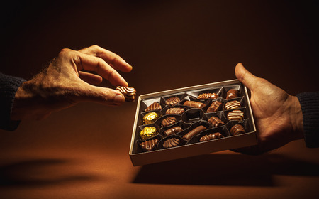 Male hands are holding an open box of chocolates and pick one.の写真素材