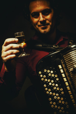 Modern accordion player posing with his chromatic harmonica type holding a glass of alcoholic drink.の写真素材