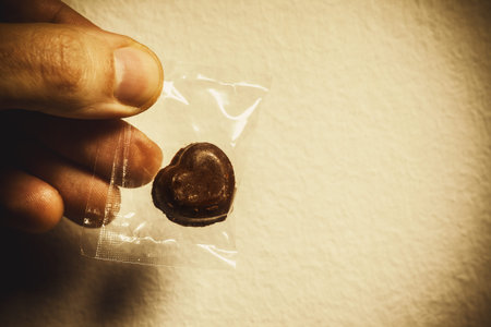 Chocolate heart wrapped in plastic bag, in male hand, conceptual composition about giving love.