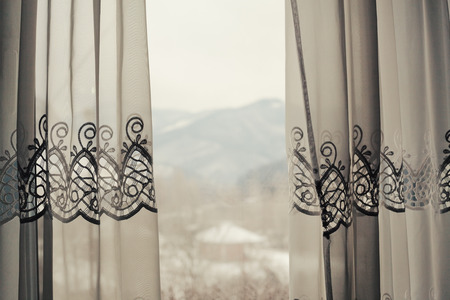 Details of a decorative curtain behind the window, winter mountain landscape in blurry background.の写真素材