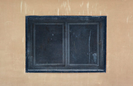 Details of a small house window covered with metal net.