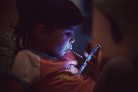 Small girl with lollipop watching a mobile phone.