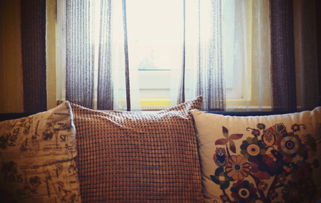 Closeup view on old decorated pillows, part of a furniture in a room in front of window.の写真素材