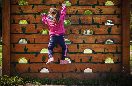 Little girl is climbing on a wooden wall in park.の写真素材