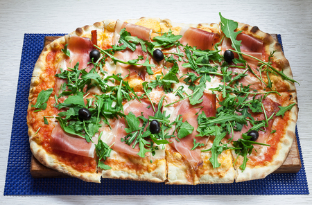 Classical pizza with ham, parsley and olives on wooden plate.の写真素材