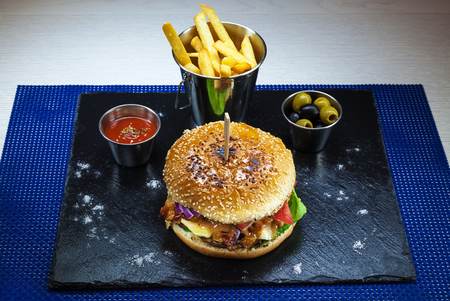 Tasty hamburger full of salad served with French fries on black ceramic plate.の写真素材