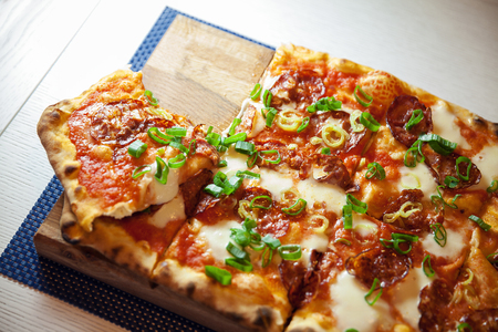 Tasty hot pizza with sausages and fresh pepper on wooden plate.の写真素材