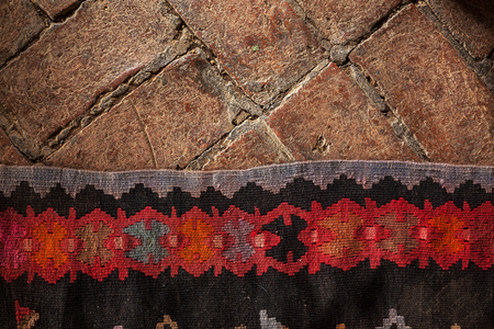 Details of an old decorative embroidery carpet on brick floor.の写真素材