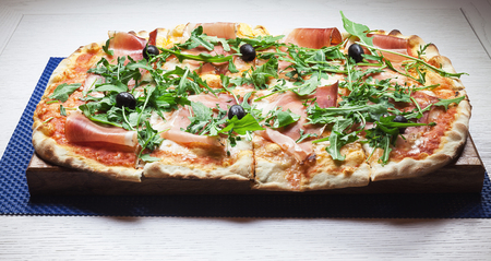 Classical pizza with ham, parsley and olives on wooden plate.の写真素材