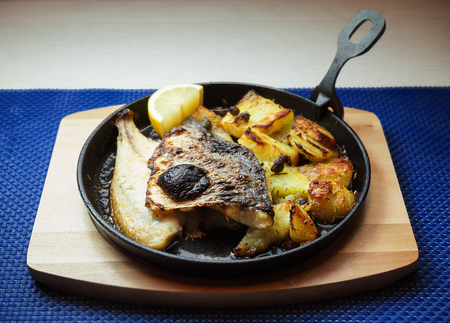 Piece of fried fish and potatoes in pan.の写真素材