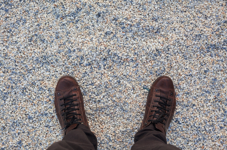 Abstract of gravel texture and two human legs wearing brown leather shoes, view from above.の写真素材