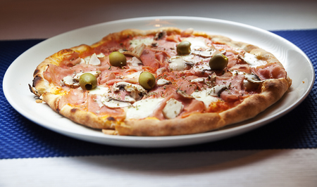 Classical pizza with ham and olives on white plate.の写真素材