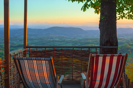 Two armchairs on wooden terrace, view on beautiful landscape during sunset, restful and peaceful place.の写真素材