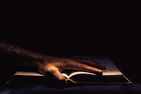Man's hand on open book, studio shot in the dark. の写真素材