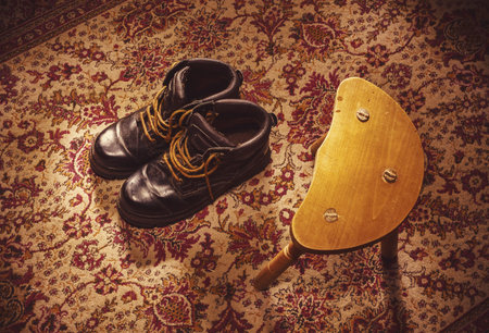Scene from ordinary life, old winter male boots on colorful carpet besides small wooden chair on...