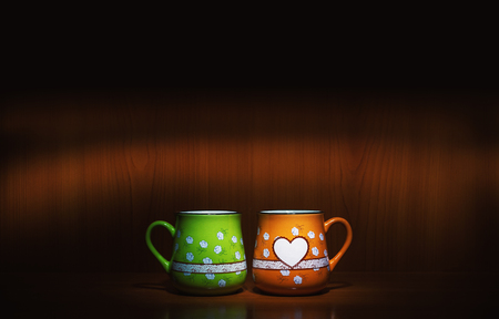 Two colorful and lovely cups, green and orange one with flower decoration and one empty heart.の写真素材