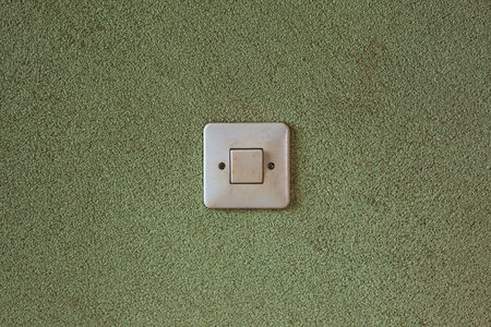 Details of an old light dirty switcher on green textured wall.