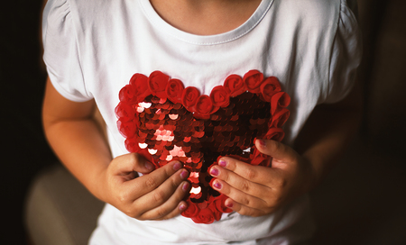 Conceptual composition, small girl holding a heart on her shirt.の写真素材
