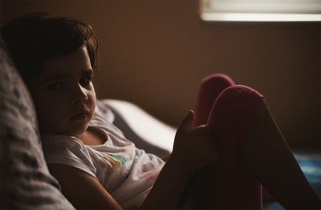 Morning scene, family life, wake up time, portrait of a small girl, laying on bed and watching to camera.の写真素材