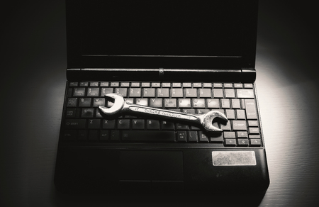 Opened old laptop on white table and metal wrench as concept of servicing.の写真素材