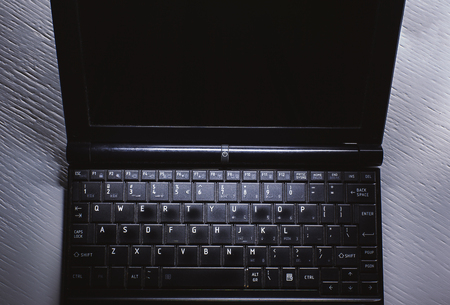 Details of a small, old and dusty laptop on white table.の写真素材