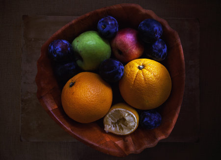 Closeup view of fresh summer fruits in dish, oranges, plums, lemon and apple.