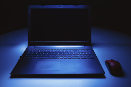 Details of a laptop and red mouse on table in the blue dark.の写真素材