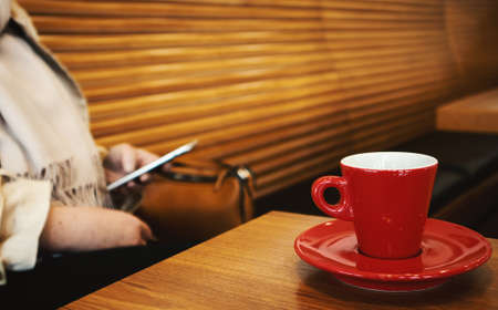 A cup of espresso coffee on the table, in the background a woman is communicating with a mobile phoneの写真素材
