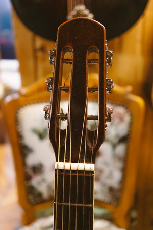 Closeup view of an old dusty acoustic guitar, details of a headstock, old vintage style chair in...