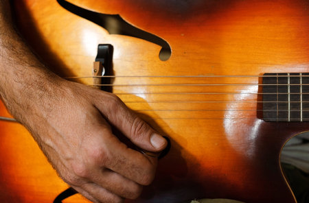 Right hand of a guitarist, ready to play on an old vintage style archtop acoustic guitar.